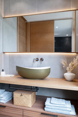 Modern and clean bathroom vanity featuring a stylish countertop washbasin on a wide wooden shelf, a large frameless mirror across the wall, and plenty of storage space below for towels and toiletries
