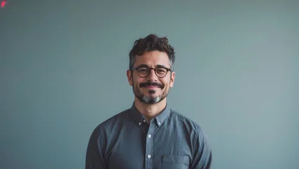Professional smiling man with glasses and beard wearing denim shirt against mint green background in modern portrait style © Ruslan Gilmanshin