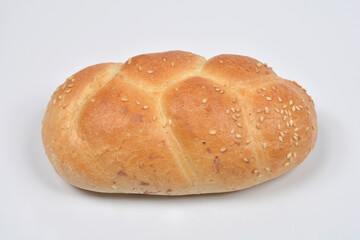 A close-up, eye-level shot of a single braided bread roll topped with sesame seeds on a white background