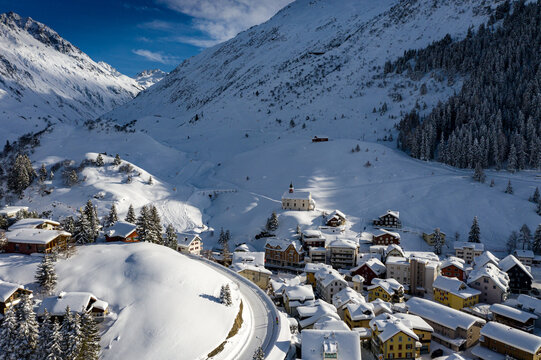 Aerial view of a small village nestled amid snow-covered hills and mountains, a solitary church perched above the rooftops, St. Anton am Arlberg, Andermatt, Switzerland