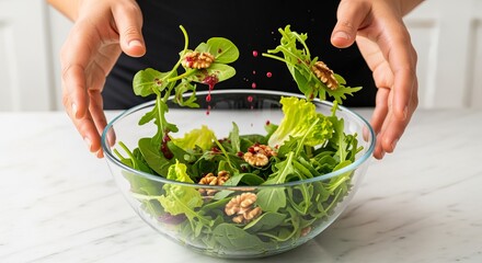 Hands tossing a fresh green salad with walnuts and dressing in a glass bowl. Close-up of food preparation with ingredients in motion. Healthy eating and nutrition concept