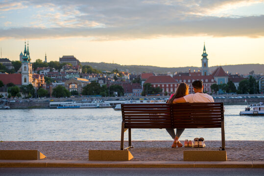 Сouple sitting on a bench by the river with their shoes off looking at old city view - Powered by Adobe
