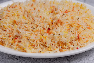 Saffron Basmati Rice – Fragrant Indian basmati rice cooked with saffron for a golden hue and aromatic flavor, served on a white plate over a textured stone background, perfect as a side dish to currie