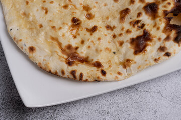 Garlic Naan Bread Traditional Indian flatbread brushed with melted butter and roasted garlic, featuring a soft, chewy texture with golden brown char marks, served on a white plate over a stone texture