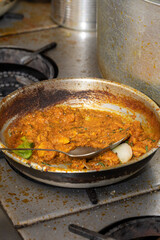 Indian Curry Cooking in Pan Authentic curry preparation on a stovetop, showing a rich, spiced sauce simmering in a metal pan with visible onions and herbs, capturing the texture, colour and aroma