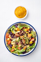 Healthy vegetable salad with lettuce, quinoa seed, azuki bean, corn, tomato, pumpkin and purple sweet potato in a bowl and pumpkin dressing on white background. Vegan and plant-based food