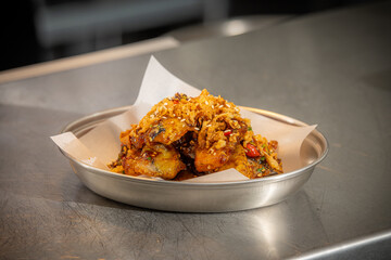 Crispy Asian Chicken Wings – Glazed chicken wings coated in a sticky sweet and spicy sauce, garnished with sesame seeds, fried onions, and chopped chili, served in a metal dish