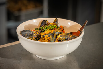 Spicy Mussel Curry – Aromatic seafood curry featuring fresh mussels cooked in a rich coconut and spice-infused sauce, garnished with green peppercorns and herbs, served in a white bowl on a counter