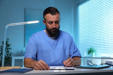 Doctor writing notes at table in clinic during night shift