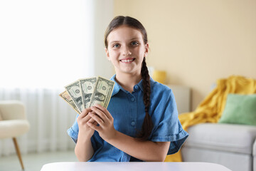 Smiling little girl with dollar banknotes at white table indoors. Pocket money