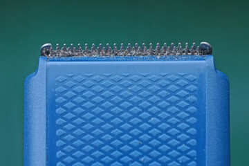 Part of one blue electric hair clipper with gray metal blades and teeth on a green background
