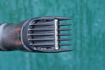 Part of one black electric hair clipper with gray metal blades and teeth on a green background