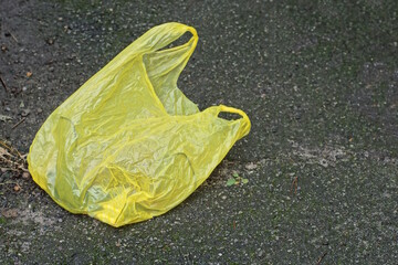trash from one empty yellow plastic bag on the gray asphalt of a summer street