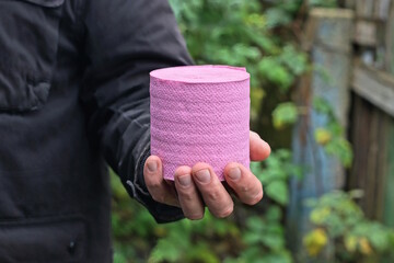 one man in black clothes holding  pink toilet paper roll in his hands on autumn street