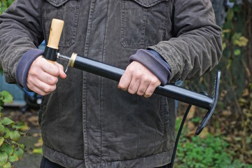 A man holding a black bicycle pump in his hand on an autumn street against the backdrop of green vegetation