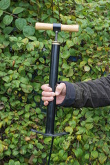 A man holding a black bicycle pump in his hand on an autumn street against the backdrop of green vegetation