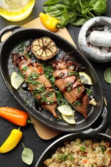 Tasty cooked squids with sauce, garlic and products on black table, flat lay