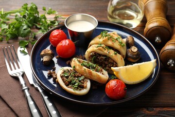 Pieces of tasty grilled squid stuffed with mushrooms, parsley, tomatoes, lemon and sauce on wooden table, closeup