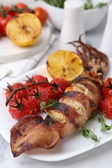 Tasty stuffed squid, microgreens, lemon and tomatoes on white marble table, closeup