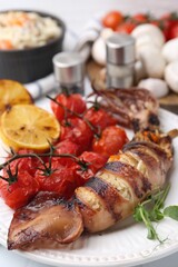 Tasty stuffed squid, microgreens, lemon and tomatoes on white table, closeup