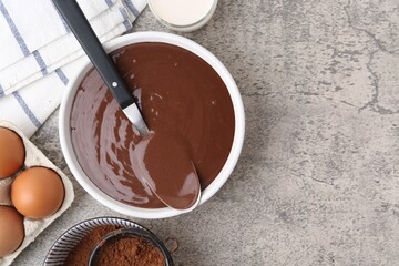 Liquid chocolate dough in bowl and ingredients on grey table, flat lay. Space for text