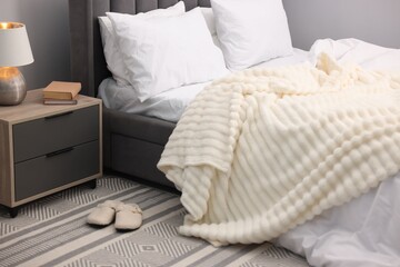 Large bed with linens, nightstand and slippers near grey wall in bedroom