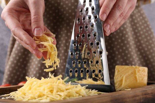 Woman with grated cheese and grater at table, closeup