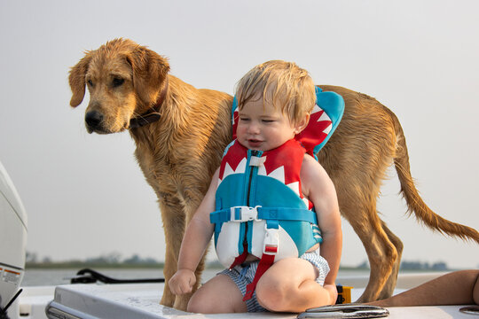Close up of a child wearing a life jacket and sitting on a boat with his dog