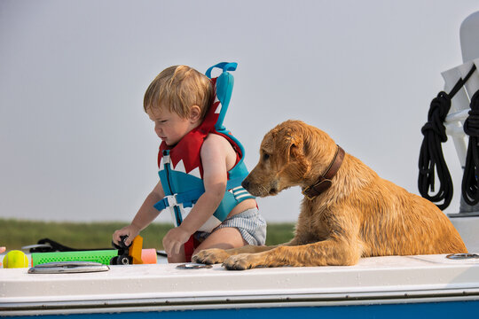 Child wearing a life jacket and playing on a boat with his dog