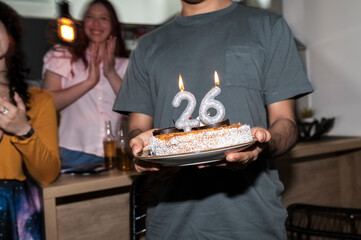 Latino man holding cake with glowing 26 candles during New Year celebration