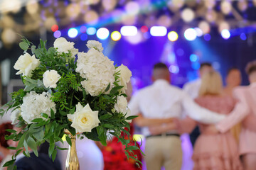 Bride's wedding bouquet and dancing couples at the wedding reception in the background.