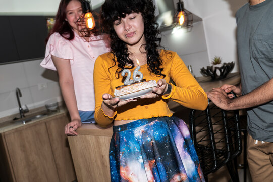 Emotional woman holding cake with 26 candles during intimate birthday party