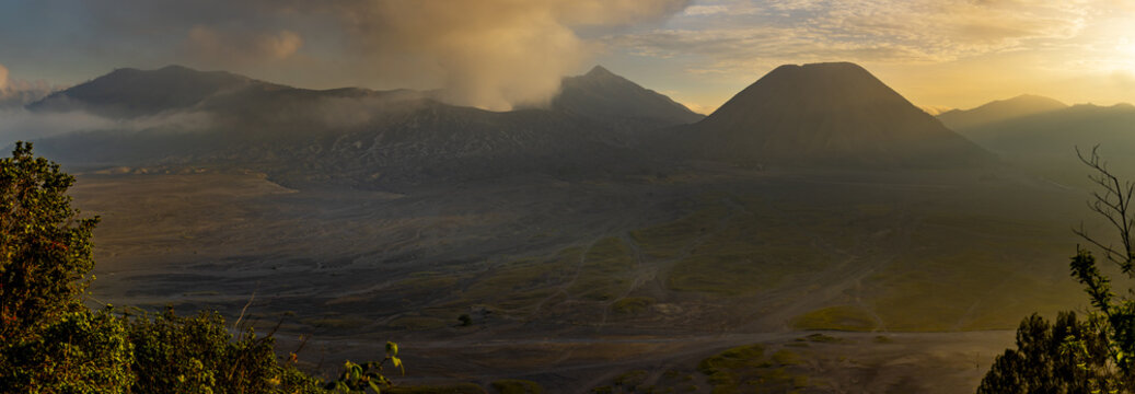 View of majestic peaks piercing through misty veils, bathed in the golden hues of sunrise, casting long shadows across the rugged terrain, Bromo, East Java, Indonesia.