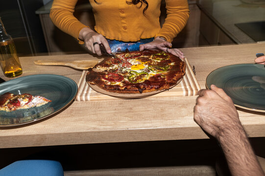 Female serving pizza slice while friends wait around kitchen table