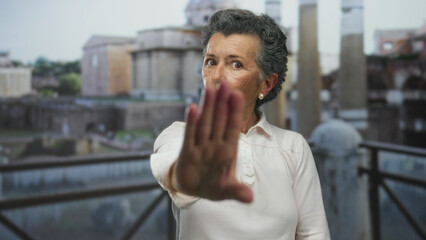 Fototapeta premium Woman with grey hair standing near roman ruins outdoor extending hand in stop gesture