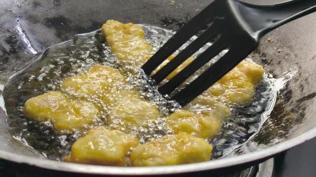 The chef is frying chicken nuggets in a wok. They are using palm oil, and the nuggets sizzle as they cook in the hot cooking oil.