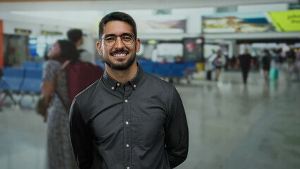 Obraz premium Young man standing confidently in a busy airport terminal with travelers in the background indicating an international travel setting.