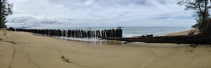A sandy beach eroded by seawater and supported by wooden posts to protect it from the waves.