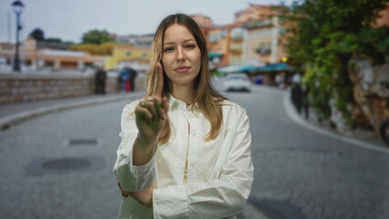 Fototapeta premium Woman pointing finger toward camera on street wearing white shirt and crossed arms; thoughtful reflection.