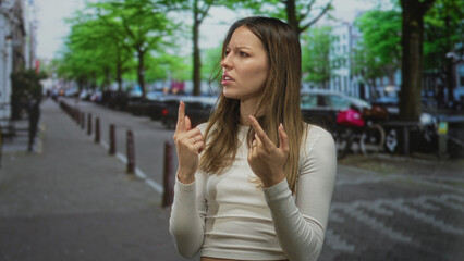 Woman finger pointing to side on a city street with raised hands and tense expression, squinting brow and pursed lips; confusion doubt.