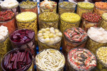 Towered rows of cylindrical jars filled with colorful pickled vegetables in brine, full-frame selection; for food design, retail promotion, packaging mockup, education.