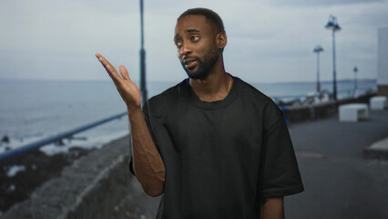 Man pointing finger up with visible forearm on a seaside street promenade near railing and...