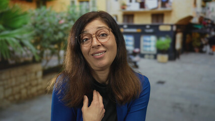 Middle age hispanic woman gestures with open palm and pointing finger to chest on city street; confusion.