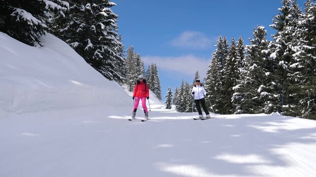 Sports female skiers in bright clothes, sliding on skis downhill on mountain background snow covered fir trees. Family vacation at ski resort on sun winter day. Front view portrait skiers skiing