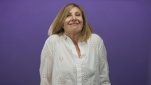 Woman wearing white eyelet blouse tilts face upward with shoulders shrugged in a purple studio; uncertainty.