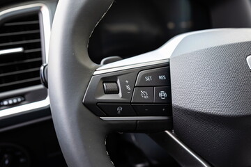 Audio volume, cruise control and various other buttons on a new car's leather wrapped steering wheel. Close up shot, no people