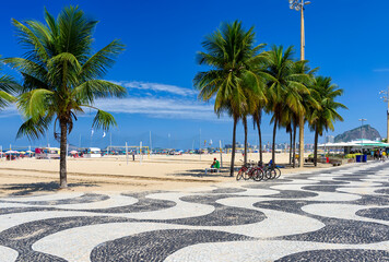 View of Copacabana beach with palms and mosaic of sidewalk in Rio de Janeiro, Brazil. Copacabana beach is the most famous beach in Rio de Janeiro. Sunny cityscape of Rio de Janeiro