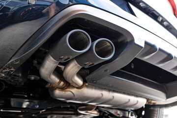 Twin tip car exhaust pipe tip and muffler, piping and silencer box on a new European car. Wide angle, looking up shot, no people