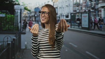 Fototapeta premium Woman smiling and beckoning with open hands wearing glasses on street near bus stop; friendly curiosity.