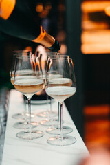 A close-up view of several glasses of champagne or white wine being poured on a marble counter during a reception.Perfect concept for celebration, luxury events, gastronomy, or hospitality visuals.
